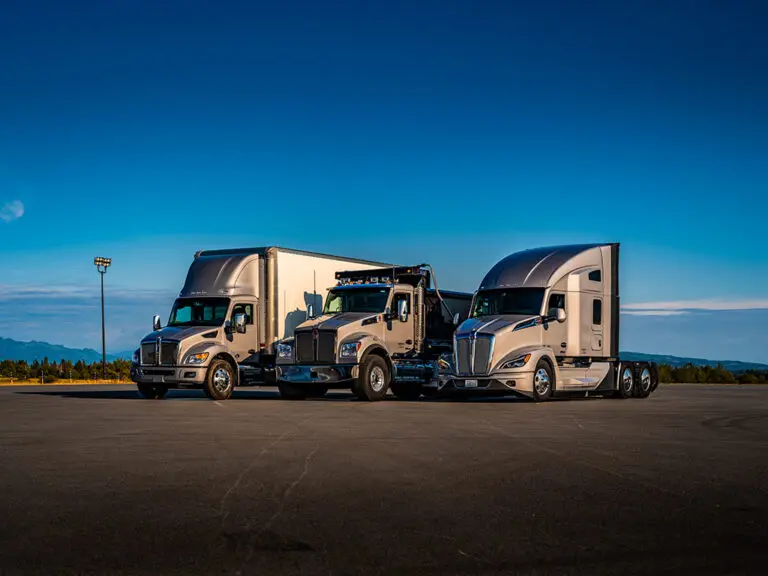Trois camions lourds Kenworth stationnés côte à côte, illustrant les véhicules diesel concernés par les nouvelles normes environnementales EPA 2027. Three Kenworth heavy-duty trucks parked side by side, representing diesel vehicles affected by the new EPA 2027 environmental standards.
