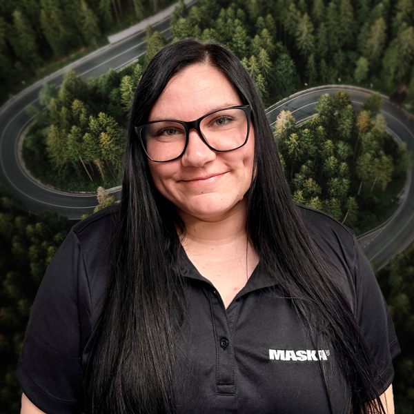 Femme portant un chandail noir MASKA, devant un décor aérien de route sinueuse traversant une forêt.